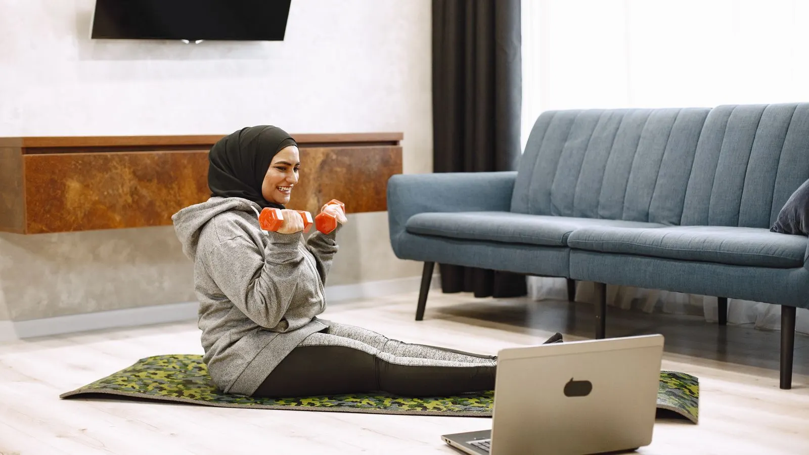 Woman training consistently at home with dumbbells and a laptop