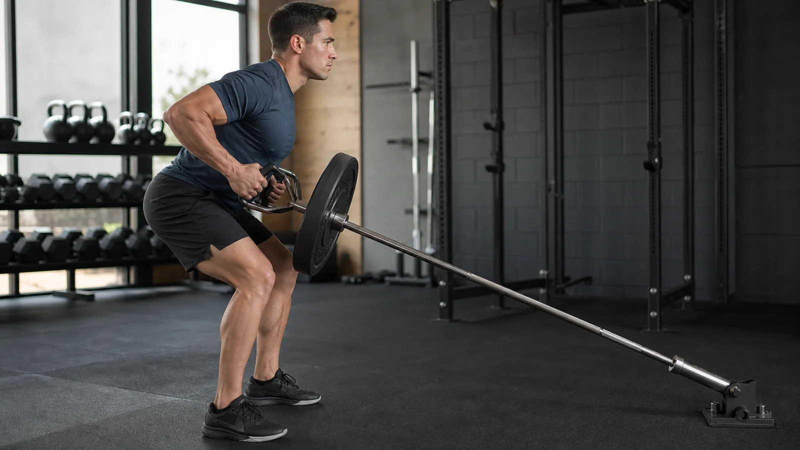 Man performing a two-arm landmine row with a barbell secured in a floor pivot